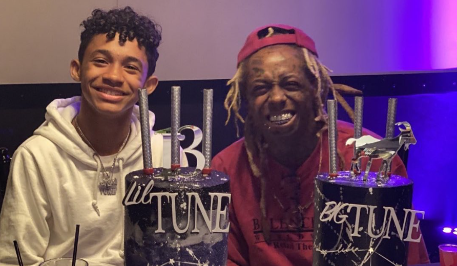Lil Wayne smiles beside his son Dwayne Carter III at a birthday celebration, with two matching cakes labeled "Lil Tune" and "Big Tune" on the table.